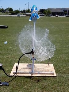 A bottle rocket blasting off with water power on a sunny day outside