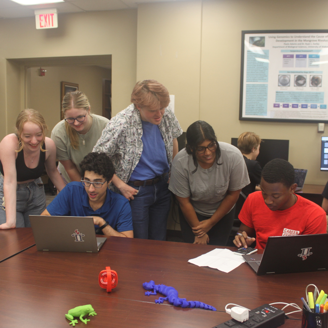 Six Randall Research Scholars gather around two of the scholars who are on laptops.