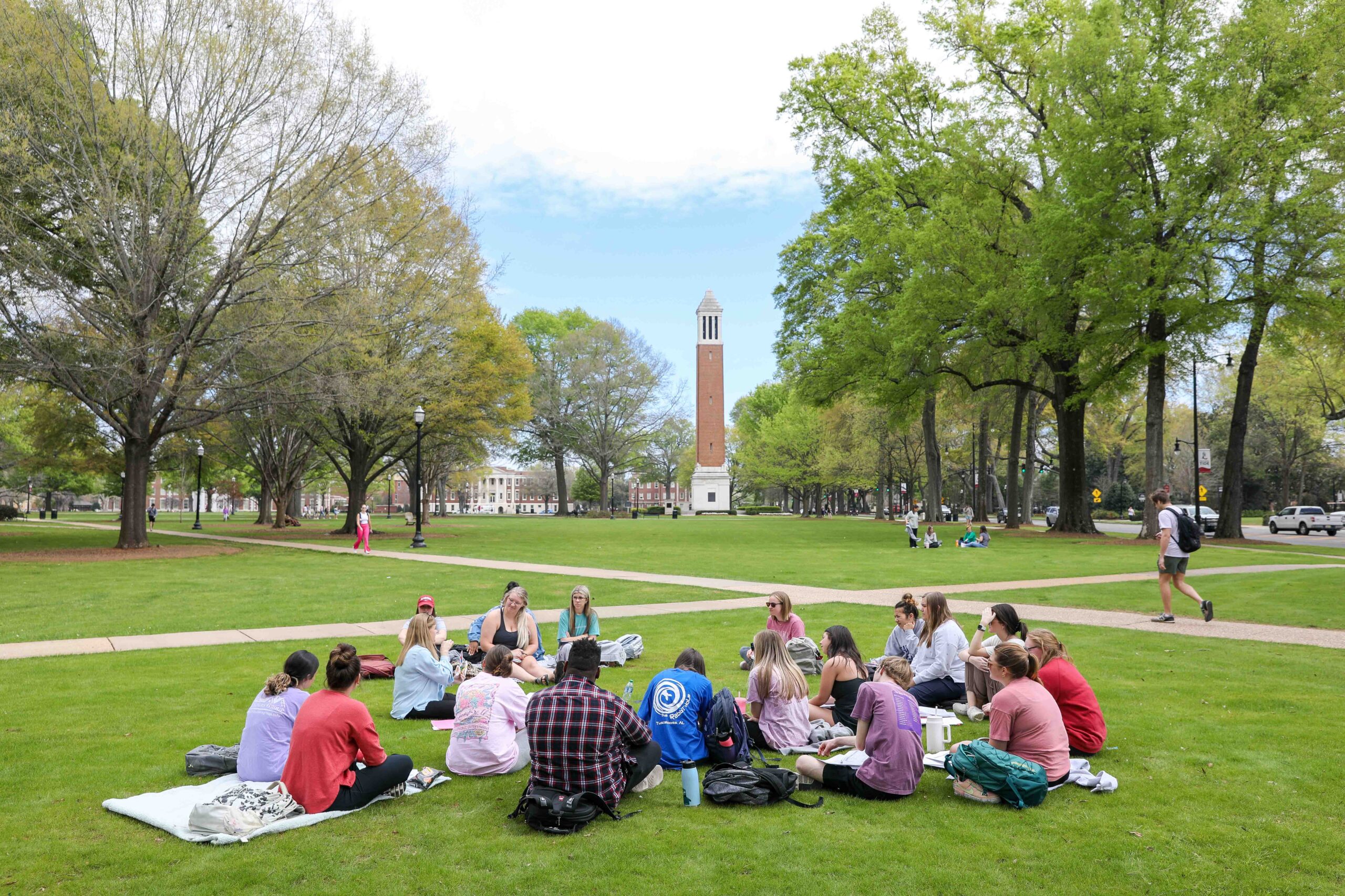 A group of students attend class outside on the quad with Denny Chimes in the background.