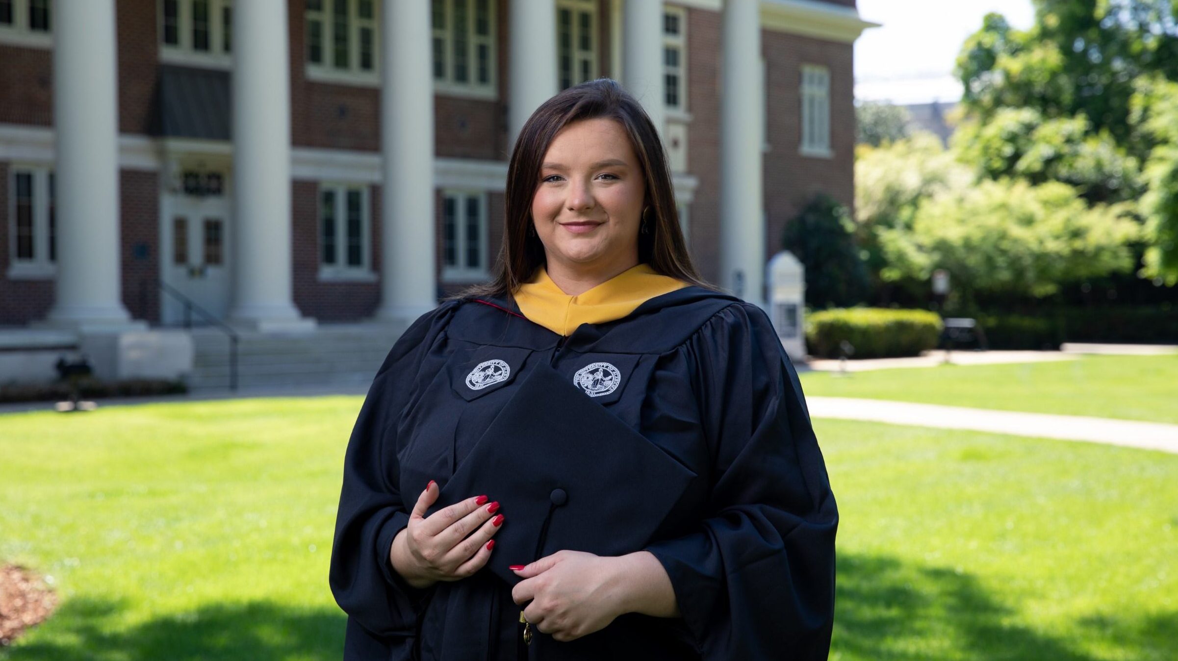 A graduate in graduation regalia smiles for the camera.