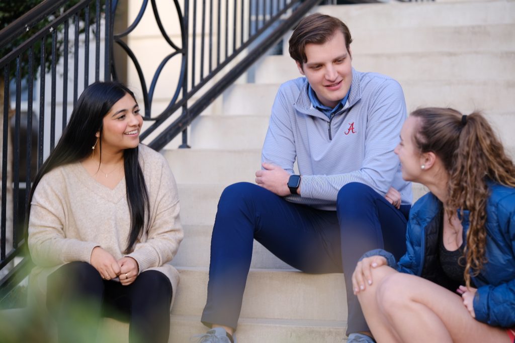 Three students sit on stairs outside and talk.