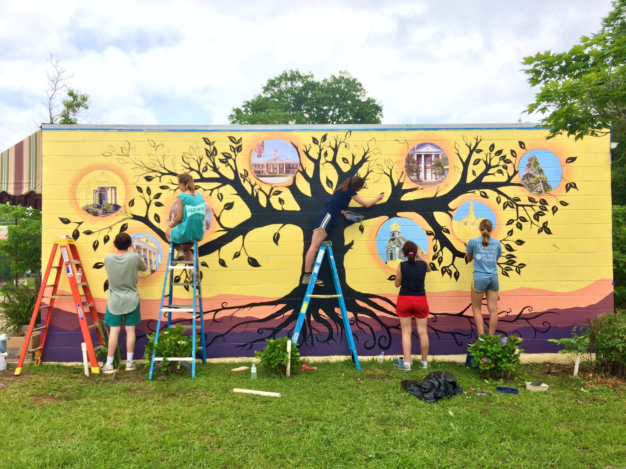 Five Witt Fellows paint a mural of a tree with landmarks on the branches.