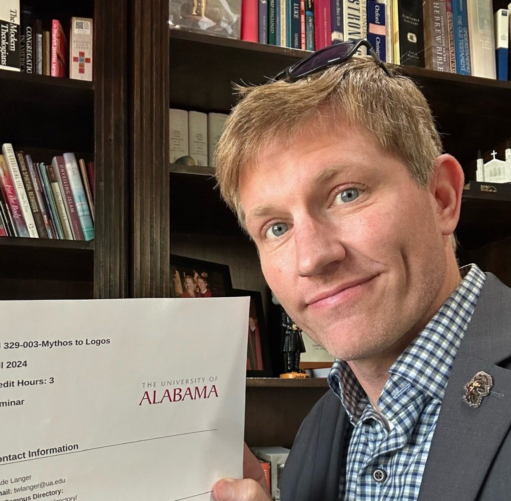 An Image of Wade Langer posing with the syllabus from his "Mythos to Logos" course.