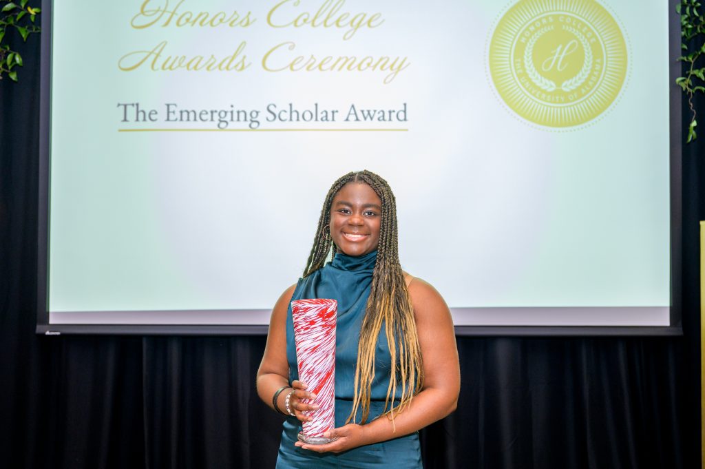 A photo of Phanuelle Manuel holding her award, a crimson and white glass vase.