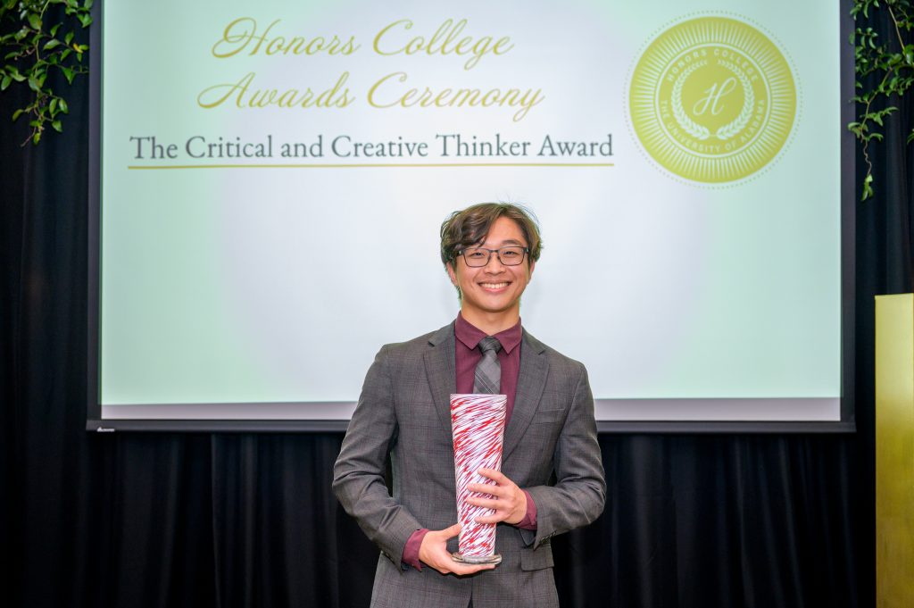 Jesse Park smiles with his award, a crimson and white glass vase.
