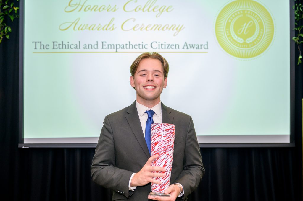 Caleb Buell smiles with his award, a crimson and white glass vase.