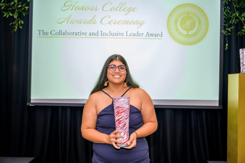 Chandni Bhat smiles with her award, a crimson and white glass vase.