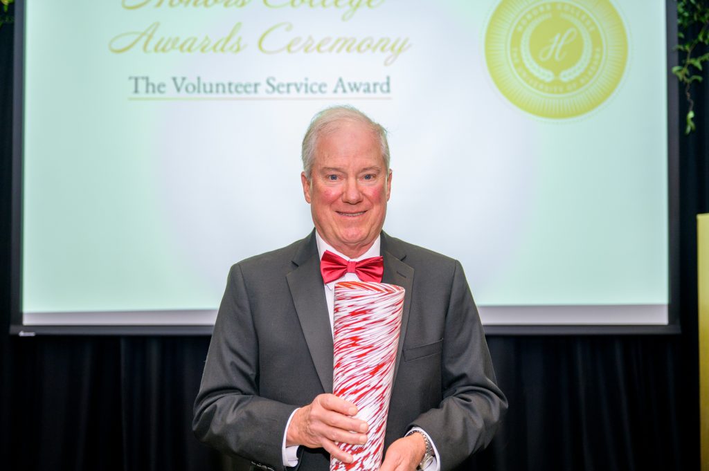 Dr. Allen Yeilding smiling while holding his award, a crimson and white glass vase.