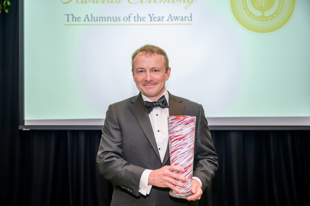 John Baschab smiles with his award, a crimson and white glass vase.